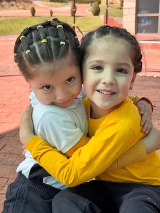 Dos niñas del nivel inicial del Colegio Horizontes se abrazan sonriendo en el patio.
