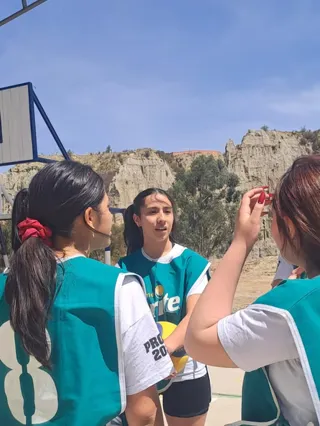 Alumnas del Colegio Horizontes con casacas deportivas conversan en la cancha al aire libre, con los cerros de La Paz de fondo.
