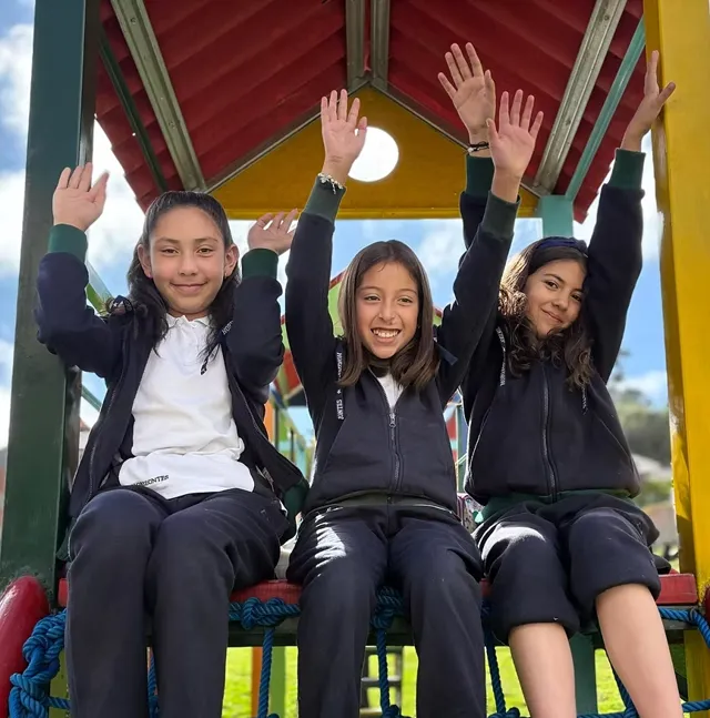 Tres alumnas del Colegio Horizontes, con el uniforme del colegio, levantan los brazos sonriendo en los juegos del patio