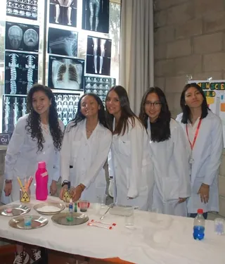 Cinco alumnas con mandil de laboratorio presentan su proyecto en la feria de ciencias del colegio