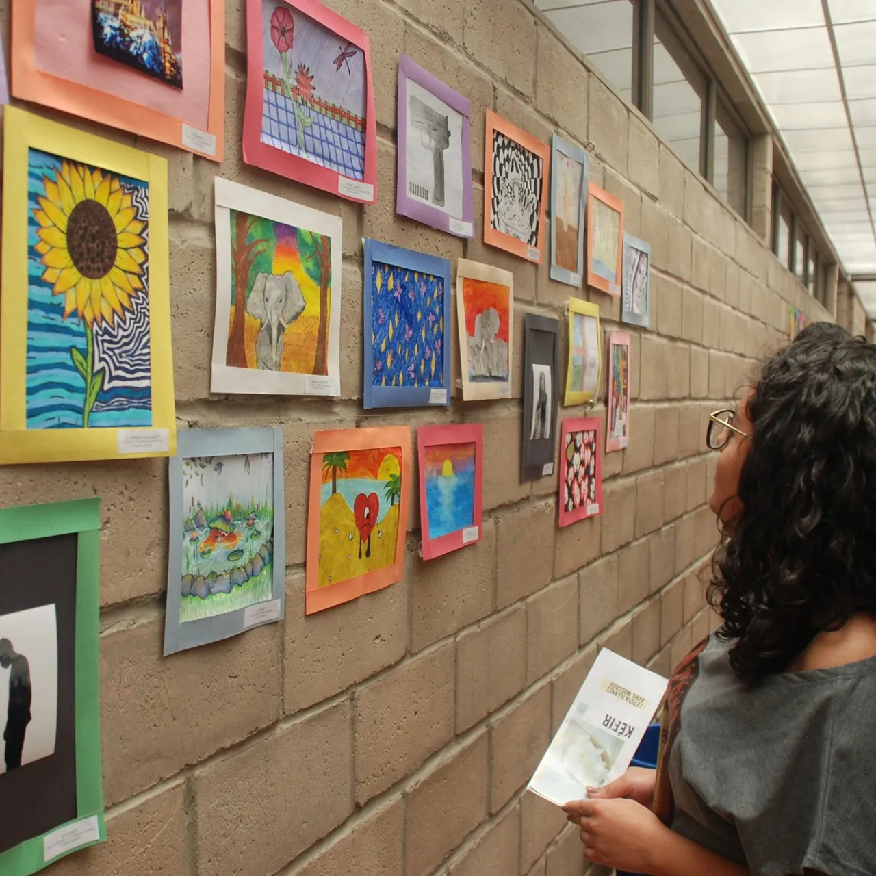 Una alumna del Colegio Horizontes observa una exposición de pinturas y dibujos coloridos realizados por las estudiantes, exhibidos en un pasillo del colegio.