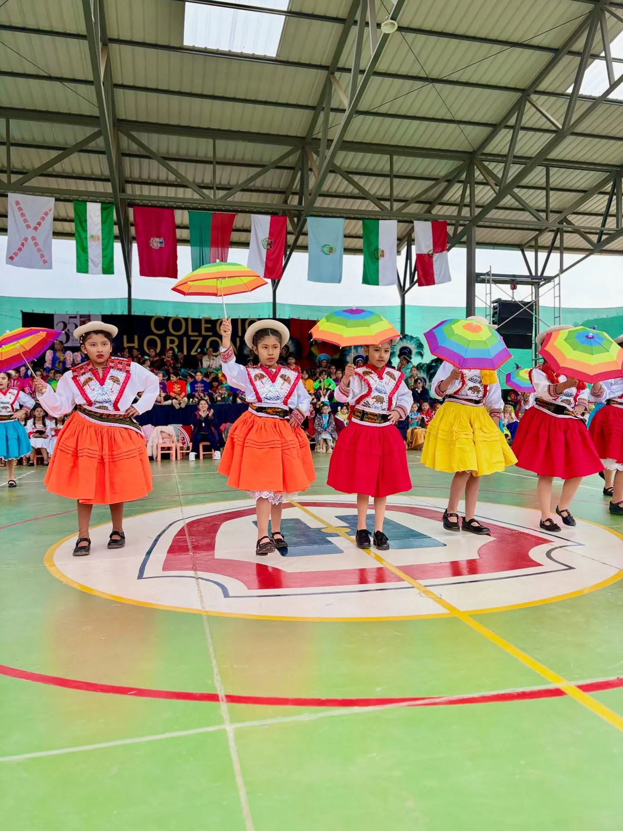 Alumnas del Colegio Horizontes bailan la danza de los Kallawayas con sombrillas multicolores sobre el piso verde de la cancha techada, durante la celebración del Día de la Familia por los 35 años del colegio.