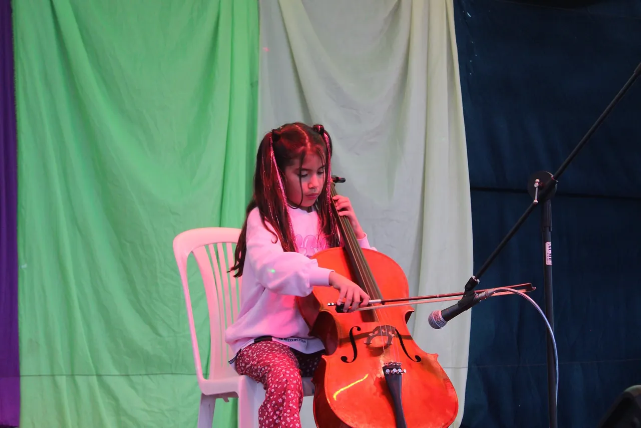 Una alumna del Colegio Horizontes toca el violonchelo, sentada sobre el escenario iluminado.