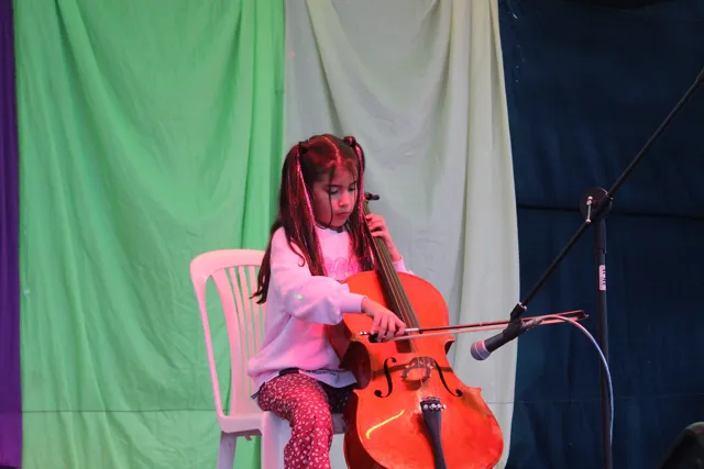 Una alumna del Colegio Horizontes toca el violonchelo, sentada sobre el escenario iluminado.