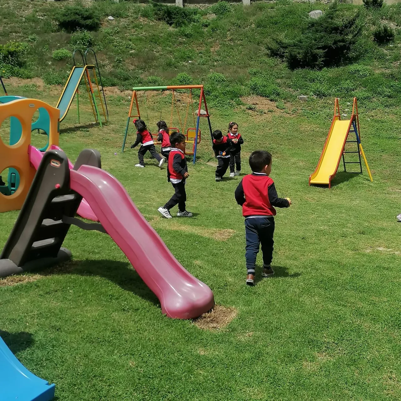 Niños y niñas del Nivel Inicial del Colegio Horizontes corren y juegan en el amplio jardín con toboganes y columpios coloridos.