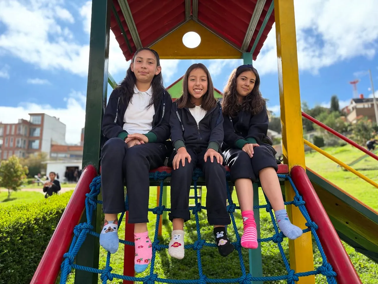 Tres alumnas del Colegio Horizontes sonríen sentadas en la estructura de juegos infantiles del jardín del colegio.