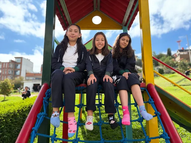 Tres alumnas del Colegio Horizontes sonríen sentadas en la estructura de juegos infantiles del jardín del colegio.