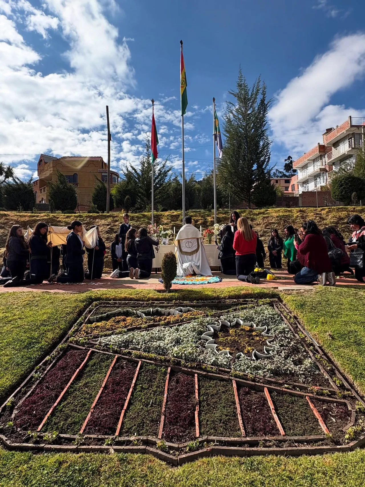 Vista del jardín del Colegio Horizontes con un macizo de flores en forma del escudo institucional, durante una ceremonia al aire libre.