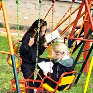 Dos alumnas del Colegio Horizontes leen sentadas en los columpios del área de juegos del colegio.