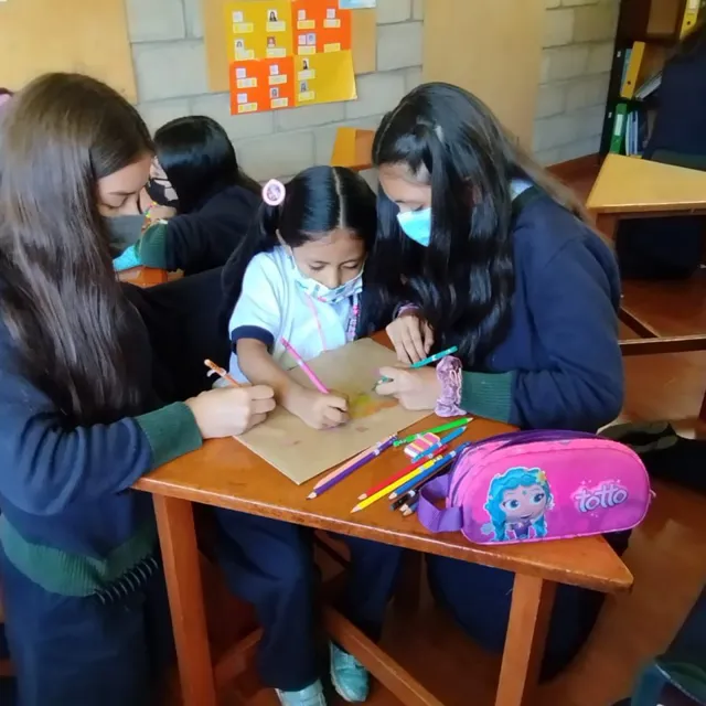 Tres alumnas del Colegio Horizontes dibujan juntas con lápices de colores sobre un escritorio en el aula de artes plásticas.