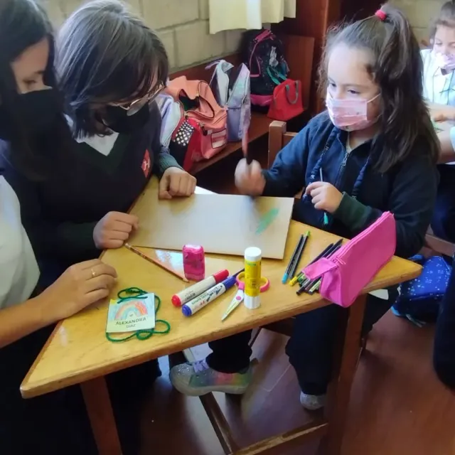 Alumnas del Colegio Horizontes trabajan con marcadores, goma y lápices de colores sobre una cartulina en el aula de artes plásticas.