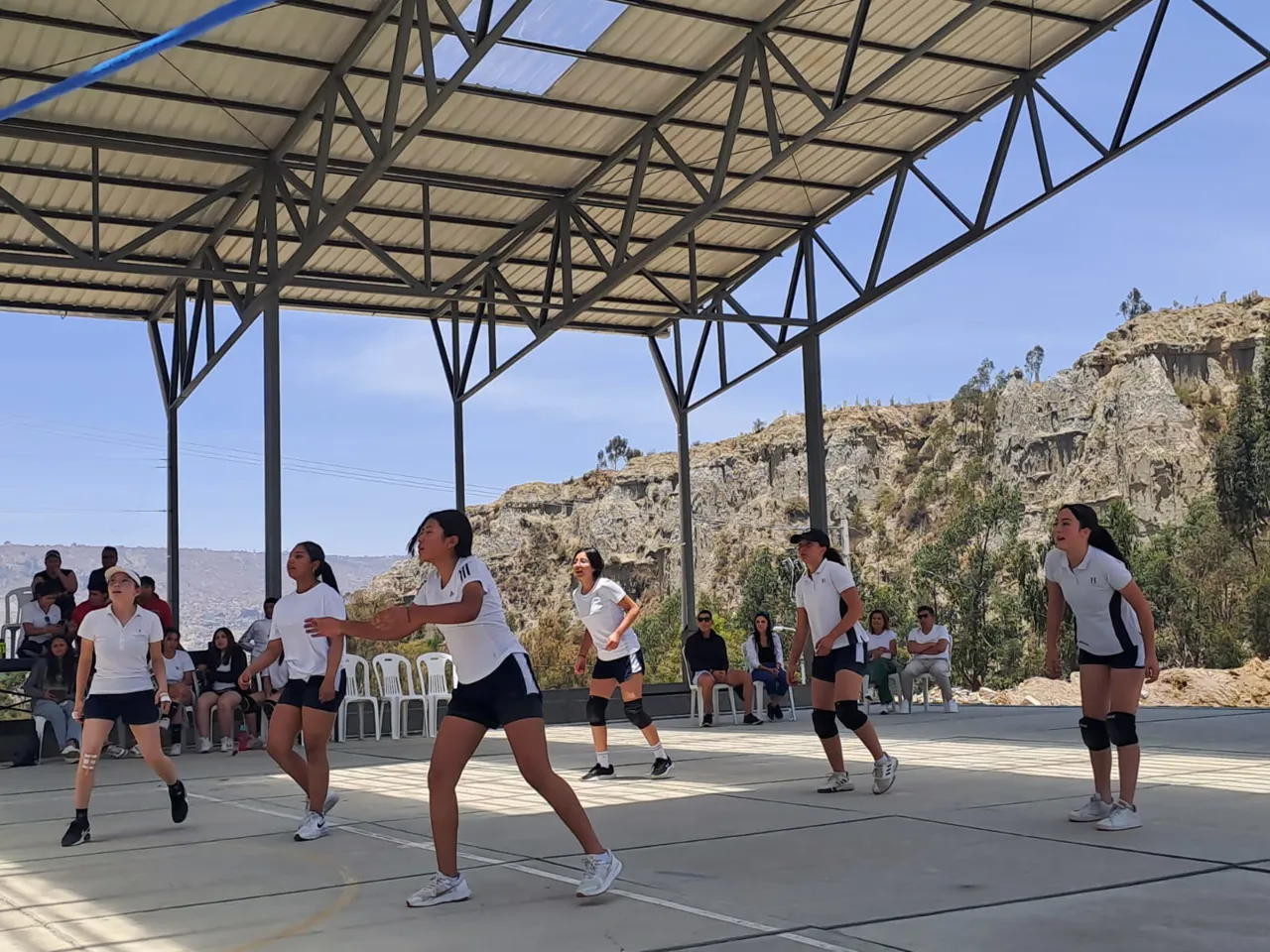 Alumnas del Colegio Horizontes disputan un partido de voleibol en la cancha techada, con las montañas de La Paz de fondo.