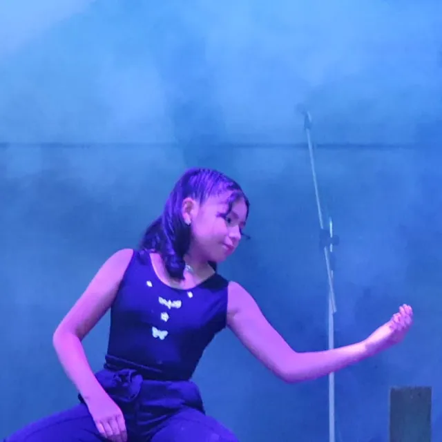 Una alumna del Colegio Horizontes canta frente al micrófono sobre el escenario, iluminada con luces azules.