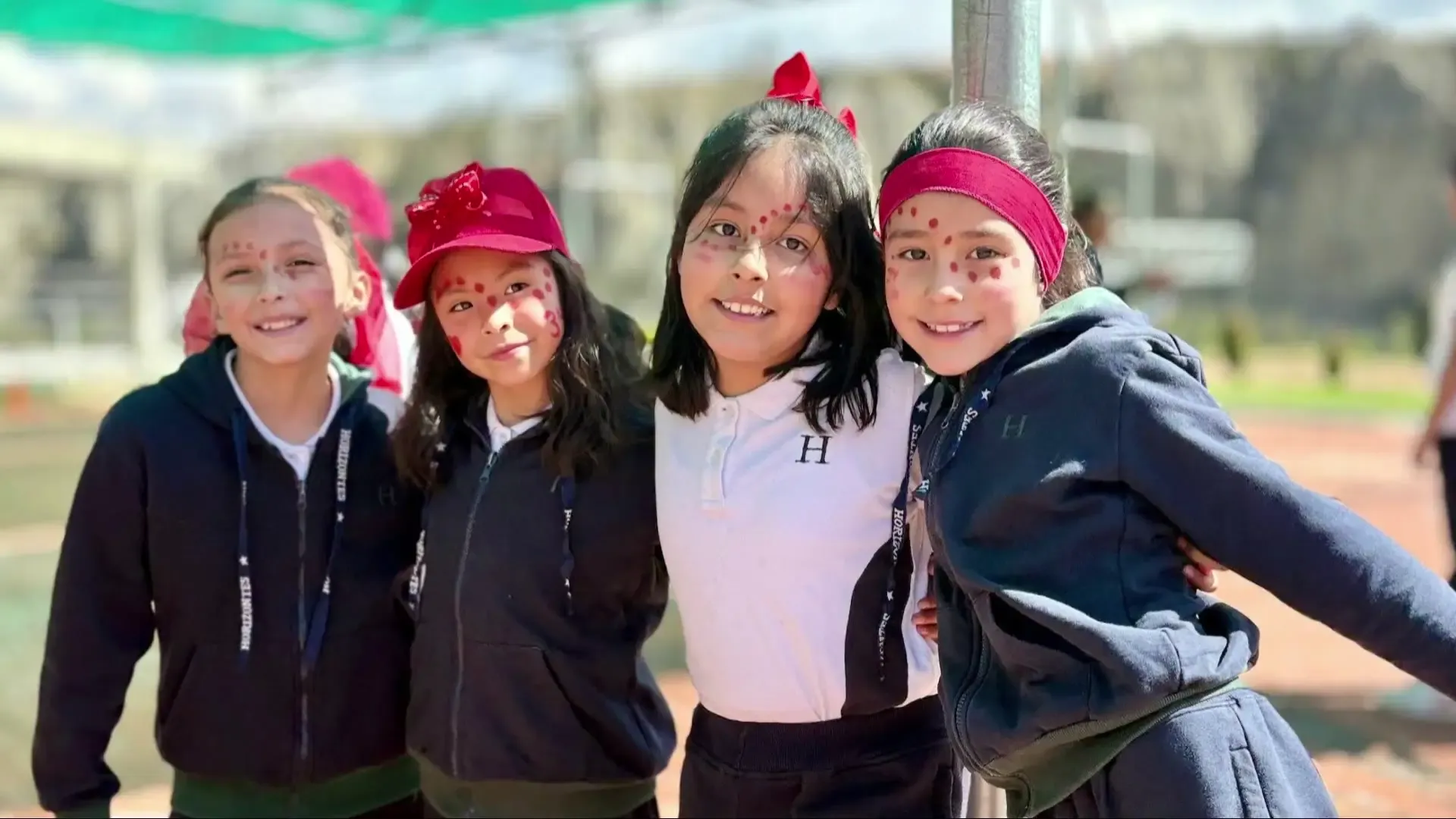 Cuatro alumnas de primaria con vinchas rojas sonríen abrazadas en el patio del Colegio Horizontes